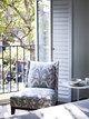 A chair upholstered in Belfour in Smoke sits elegantly by French doors, offering a view of the balcony. The soft, rhythmic pattern of the fabric complements the serene outdoor scene, inviting moments of relaxation and reflection.